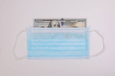 Amerikan Doları kağıt para. Beyaz arka planda cerrahi antivirüs maskesinden geçen 100 dolarlık banknot.