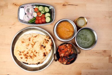 Baharatlı kırmızı tavuk ızgara tikka tandır nan ekmeği yeşil ıspanak körili yoğurt sosu domates salatalıklı soğan salatası metal paslanmaz çelik pirinç pirinç pirinç bakır kap hafif ahşap zemin üzerinde