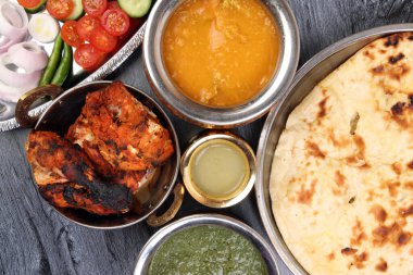 Baharatlı kırmızı tavuk ızgara tikka tandır nan ekmeği yeşil ıspanak körili yoğurt sosu domates salatalığı soğan salatası metal paslanmaz çelik pirinç pirinç pirinç bakır kap siyah ahşap arka plan