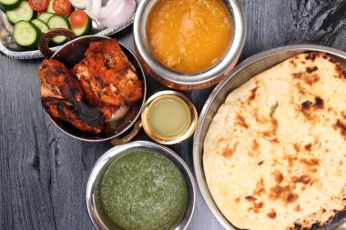 Baharatlı kırmızı tavuk ızgara tikka tandır nan ekmeği yeşil ıspanak körili yoğurt sosu domates salatalığı soğan salatası metal paslanmaz çelik pirinç pirinç pirinç bakır kap siyah ahşap arka plan