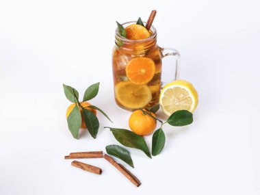 Yeşil yapraklı tarçınlı limonlu portakal çayı şeffaf cam kavanozda çubuk beyaz arka planda bütün meyve.