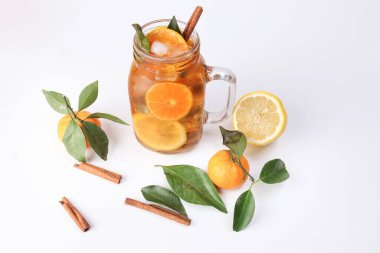 Yeşil yapraklı tarçınlı limonlu portakal çayı şeffaf cam kavanozda çubuk beyaz arka planda bütün meyve.