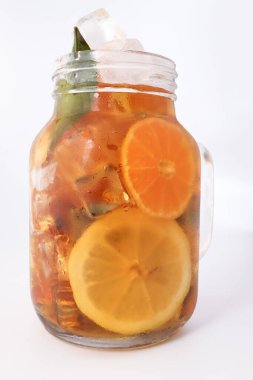 Yeşil yapraklı tarçınlı limonlu portakal çayı şeffaf cam kavanoz bardakta beyaz arka planda.