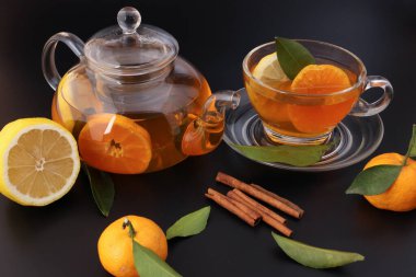 Likit çay, portakal dilimi yeşil yaprak tarçın şeffaf cam çay fincanı çay fincanı çaydanlığı, siyah arka planda.