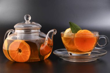 Likit çay, portakal dilimi yeşil yaprak tarçın şeffaf cam çay fincanı çay fincanı çaydanlığı, siyah arka planda.