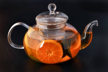 Likit çay, portakal dilimi yeşil yaprak tarçın şeffaf cam çaydanlık, siyah arkaplan.