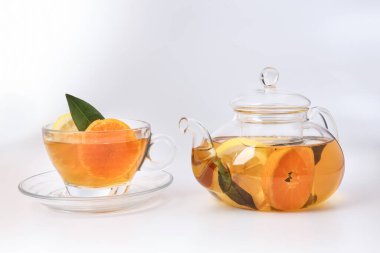 Likit çay portakal dilimi yeşil yaprak tarçın şeffaf cam çay fincanı çay fincanı demliği beyaz arka planda.
