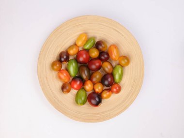 Kırmızı turuncu yeşil domates, beyaz arka plan üzerinde ahşap tabakta karışıyor.