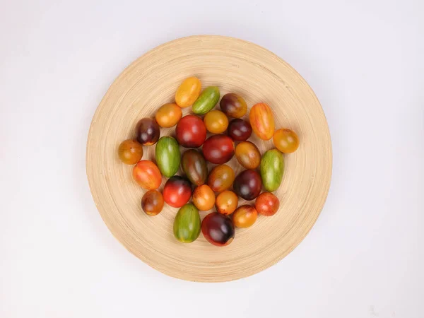 Red orange yellow green tomato mix variety on wooden plate over white background