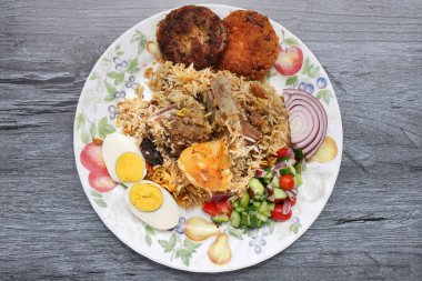 Ev usulü kacchi biryani ile patates pirzolası, salatalık, soğan salatası ve eski usul ahşap kaplama.