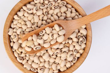 Tahta kâse içindeki siyah fasulye kaşığı beyaz arka planda üstten görünüyor.