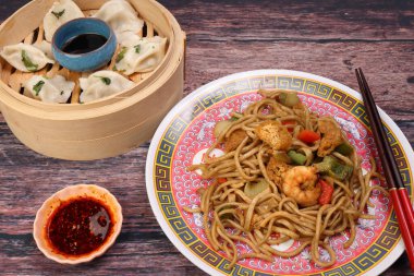 Bambu buharlı, biberli, biberli hamur tatlısı karidesli, deniz mahsullü tofu biberli kızarmış şehriye, doğu tarzı tabak çubukları ve rustik ahşap arka plan.