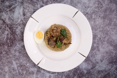 Biryani Tehari, kaynamış yumurta kişniş yaprağıyla kaynamış yağda pişirilmiş beyaz tabakta rustik mermer mermer arka planda garnitür yapıyor.