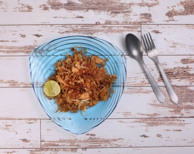 Tayland usulü sahanda kızartılmış pirinç erişteli Tayland yemeği. Kırsal ahşap arka planda mavi camdan bir çatal kaşığın üzerinde.