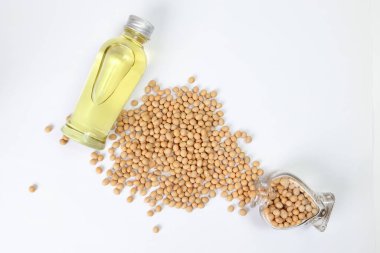 Soyabetliler beyaz arka planda soya fasulyesi yağı şişesinin etrafına Hart şeklindeki cam şişeden döküyorlar.