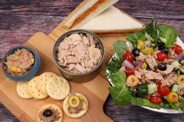 Tin can tuna fish meat chunk flake product recipes salad spread topping tapas cracker sandwich on wooden black slate board over rustic wooden table