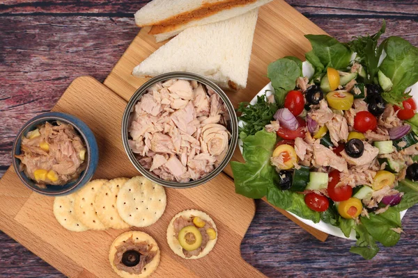 Tin can tuna fish meat chunk flake product recipes salad spread topping tapas cracker sandwich on wooden black slate board over rustic wooden table