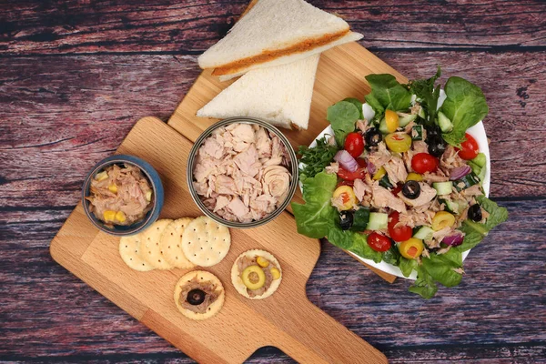 Tin can tuna fish meat chunk flake product recipes salad spread topping tapas cracker sandwich on wooden black slate board over rustic wooden table