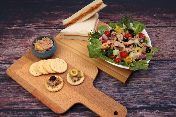 Tin can tuna fish meat chunk flake product recipes salad spread topping tapas cracker sandwich on wooden black slate board over rustic wooden table