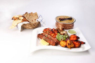 Karışık ızgara kebap tavuk sığır eti karides naneli balık limon salamura soğan ekmeği chapati naan tandoori dal mercimek kızarmış tadka bakır kap beyaz arka planda