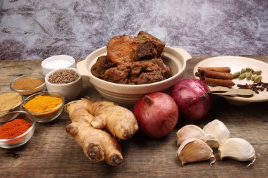 Biftek bhuna kuru köri, seramik kasede patates, biber, kimyon, kişniş, zerdeçal, sarımsak, zencefil, tarçın, kakule, ahşap arka planda karanfil.