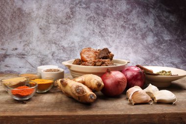 Biftek bhuna kuru köri, seramik kasede patates, biber, kimyon, kişniş, zerdeçal, sarımsak, zencefil, tarçın, kakule, ahşap arka planda karanfil.