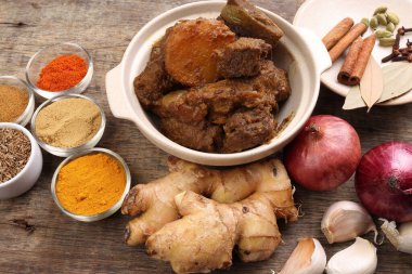 Biftek bhuna kuru köri, seramik kasede patates, biber, kimyon, kişniş, zerdeçal, sarımsak, zencefil, tarçın, kakule, ahşap arka planda karanfil.