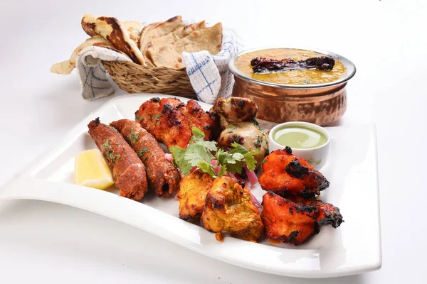 Karışık ızgara kebap tavuk sığır eti karides naneli balık limon salamura soğan ekmeği chapati naan tandoori dal mercimek kızarmış tadka bakır kap beyaz arka planda