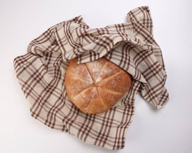 Kareli mutfak kumaşına sarılı taze pişmiş yuvarlak ekmek beyaz zemin üzerine peçete havlusu.