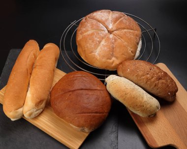 Taze pişmiş ekmek ekmeği rulo etrafında uzun karışık verity ahşap tahta metal ızgara üzerinde siyah arka plan üzerinde