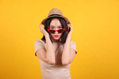Güzel genç Güneydoğu Asyalı kadın kırmızı çerçeveli güneş gözlüklü şapka moda zirvesi sarı turuncu arka planda mutlu kafanın arkasında.