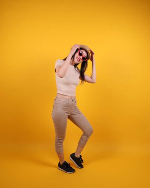 Güzel, genç, Güneydoğu Asyalı kadın kırmızı çerçeveli, güneş gözlüklü, poz veren sarı arka planda yürü.