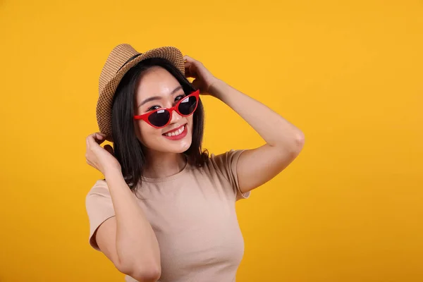 Beautiful young south east Asian woman red frame sunglass hat pose style fashion peak happy on yellow orange background hand behind head pull