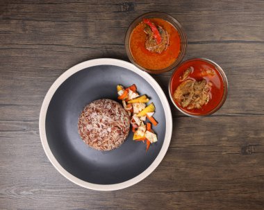 Nasi dagang özel kahverengi pirinç hindistan cevizi sütü ile pişirilmiş sebze turşulu ananas havucu ve siyah açık beyaz tabak tavuklu köri tabağı, siyah ahşap arka planda.