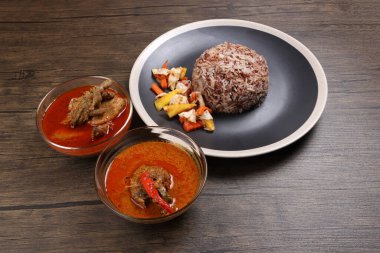 Nasi dagang özel kahverengi pirinç hindistan cevizi sütü ile pişirilmiş sebze turşulu ananas havucu ve siyah açık beyaz tabak tavuklu köri tabağı, siyah ahşap arka planda.