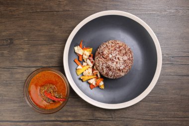 Nasi dagang özel kahverengi pirinç hindistan cevizi sütü ile pişirilmiş sebze turşulu ananas havucu beyaz tabak balığının köri kabı içinde koyu ahşap arka planda.