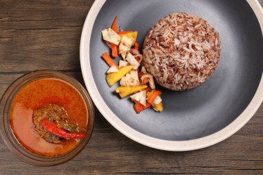 Nasi dagang özel kahverengi pirinç hindistan cevizi sütü ile pişirilmiş sebze turşulu ananas havucu beyaz tabak balığının köri kabı içinde koyu ahşap arka planda.