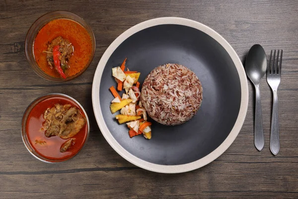 Nasi dagang 'ın özel kahverengi pirinci hindistan cevizi sütü, sebze turşusu, havuç, siyah açık beyaz tabak, balık, köri kasesi, ahşap arka plan kaşığıyla pişiriliyor.