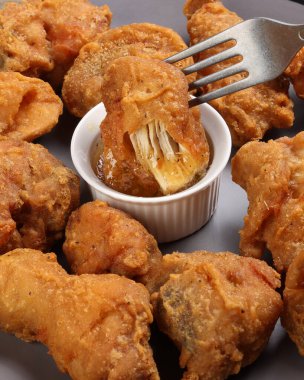 Hafif yağda kızartılmış tavuk karışımı parçalar çataldan damlayan gri tabağa sarımsak damlatan yumuşak bir sos ahşap arka planda.