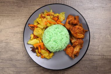 Steamed green rice spiced deep fried chicken cabbage carrot vegetable warung nasi ayam goreng on dark grey plate wooden background clipart