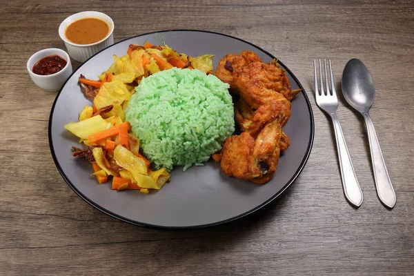 Steamed green rice spiced deep fried chicken cabbage carrot vegetable warung nasi ayam goreng on dark grey plate wooden background gravy sambal sauce fork spoon — Stock Image Steamed Green Rice Spiced Deep Fried Chicken Cabbage Carrot Vegetable Stock Picture