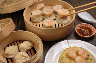 Karidesli shaomai pick by chopsticks Xiao long bao dim sum hamur köftesi karidesli balık karides bambu buharlı deniz mahsulü sebze pilavı tabak soslu çorba kaşığı üzerinde rustik arka plan üzerinde kızartılmış pirinç