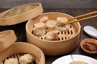 Karidesli shaomai pick by chopsticks Xiao long bao dim sum hamur köftesi karidesli balık karides bambu buharlı deniz mahsulü sebze pilavı tabak soslu çorba kaşığı üzerinde rustik arka plan üzerinde kızartılmış pirinç