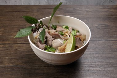 Vietnam poh bifteği erişte çorbası biftek köftesi, işkembe, mide parçaları ahşap masa üzerinde kasede Tayland fesleğeni limonu filizlenmiştir.