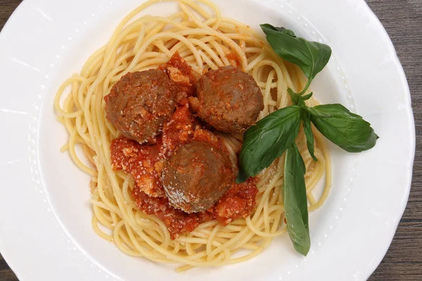 Cooked spaghetti tomato meatball sauce cheese powder basil on white plate wooden table