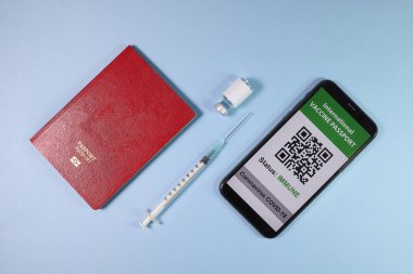 Dijital uluslararası aşı pasaport akıllı telefon ekranı QR kod uygulaması Coronavirus covid 19 bağışıklık sistemi kırmızı pasaport küçük şişe tek kullanımlık tıbbi şırınga açık mavi arka planda