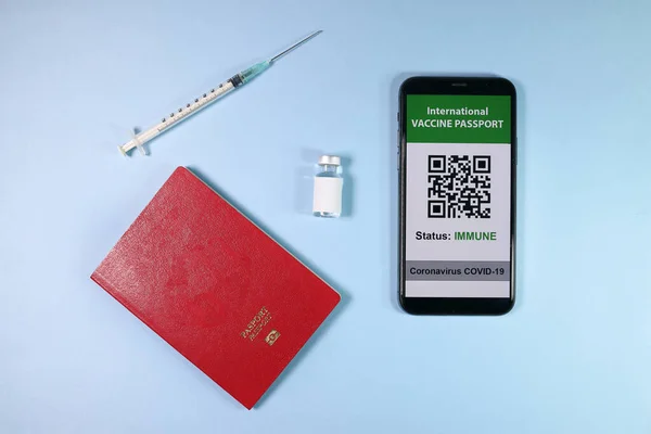 Dijital uluslararası aşı pasaport akıllı telefon ekranı QR kod uygulaması Coronavirus covid 19 bağışıklık sistemi kırmızı pasaport küçük şişe tek kullanımlık tıbbi şırınga açık mavi arka planda
