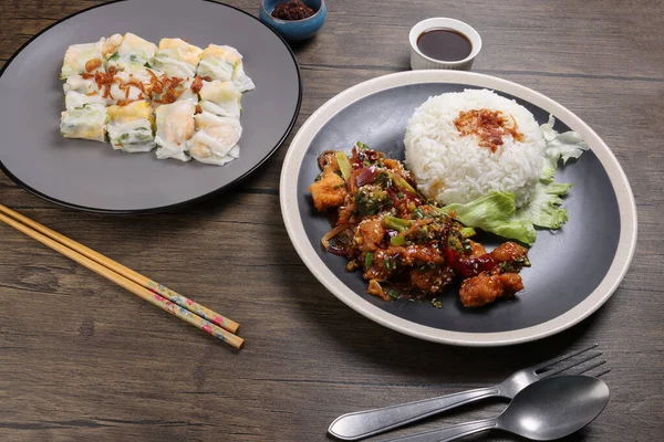 Chinese style Kung Pao Gong Bao Kung Po stair fried chicken and rice noodle roll cheung fun stuffed shrimp chicken vegetable on dark plate sauce fork spoon chopsticks on rustic dark wood table — Stock Image Chinese Style Kung Pao Gong Bao Kung Stair Fried Chicken Royalty Free Stock Images