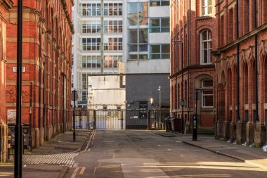 Manchester, İngiltere, Mart 04, 2024: Tarihi kırmızı tuğla binalar ve modern mimari tarafından çerçevelenmiş boş kentsel cadde. Sakin şehir atmosferi sanayi mirası ve çağdaş şehir yaşamını vurguluyor.