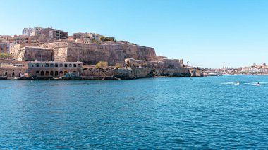 Valletta, Malta - 8 Nisan 2024: Valletta 'nın tarihi kireçtaşı tahkimatı ve liman limanını Sliema' dan gelen feribot rotasından, turkuaz Akdeniz suyu ve temiz bir gökyüzü altında küçük teknelerle geniş açıdan görmek
